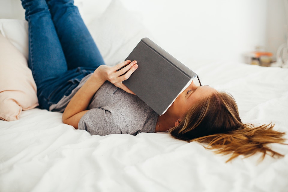 woman lying on bed holding book